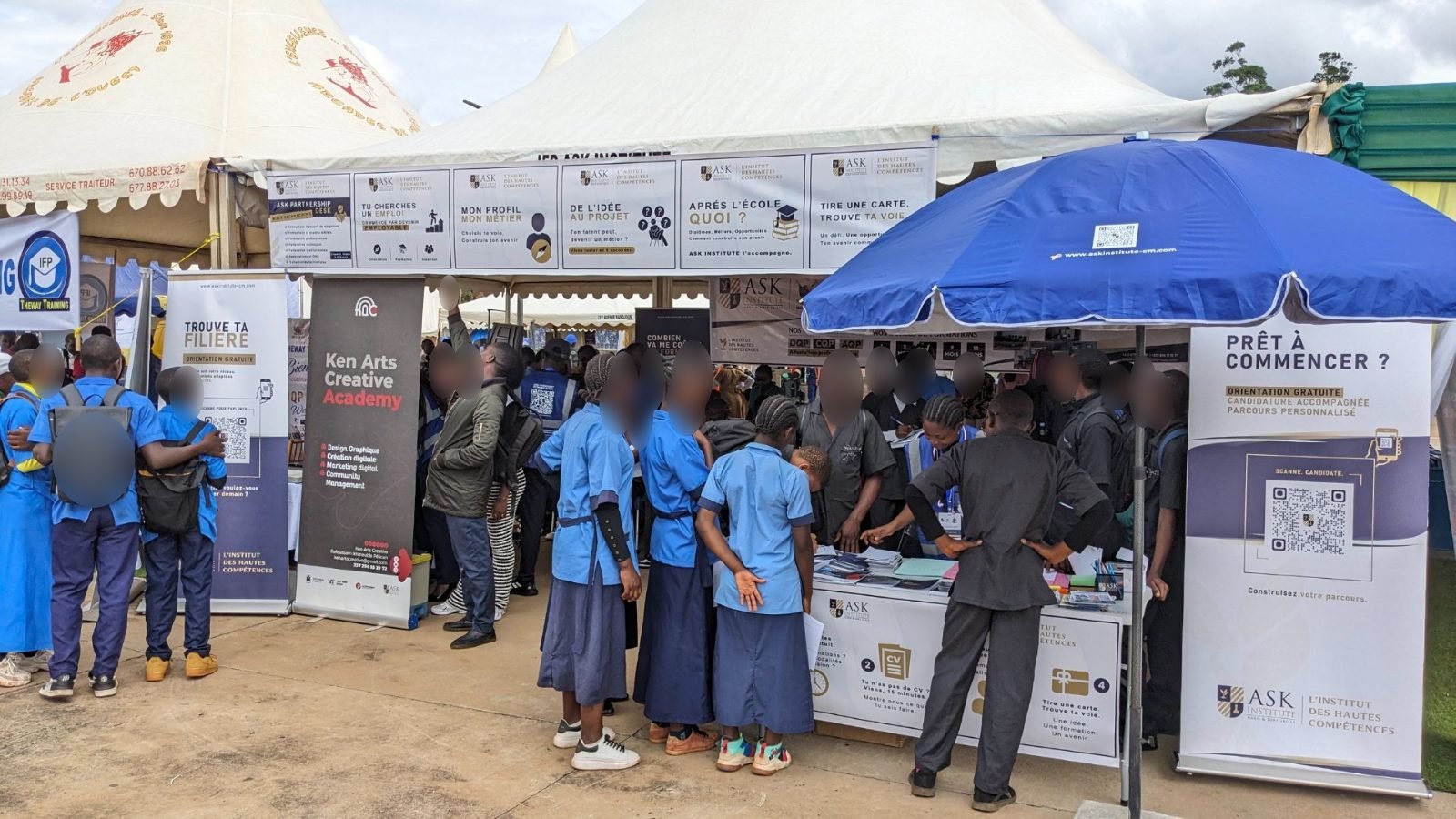 Le stand de ASK au CAMBE Ouest 2026, sous une tente et un parasol bleu : des élèves en uniforme se pressent autour des tables, entre les kakémonos « Trouve ta spécialité » et « Prêt à commencer ? ».