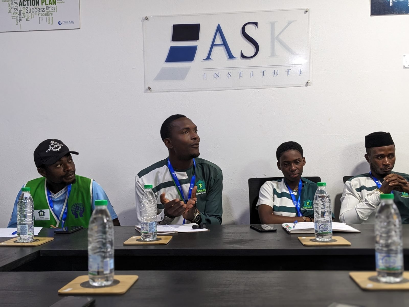 Quatre participants de la CECAEC COOP-CA assis à la table de formation, sous l’enseigne de ASK Institute ; l’un d’eux s’exprime pendant que les autres l’écoutent.