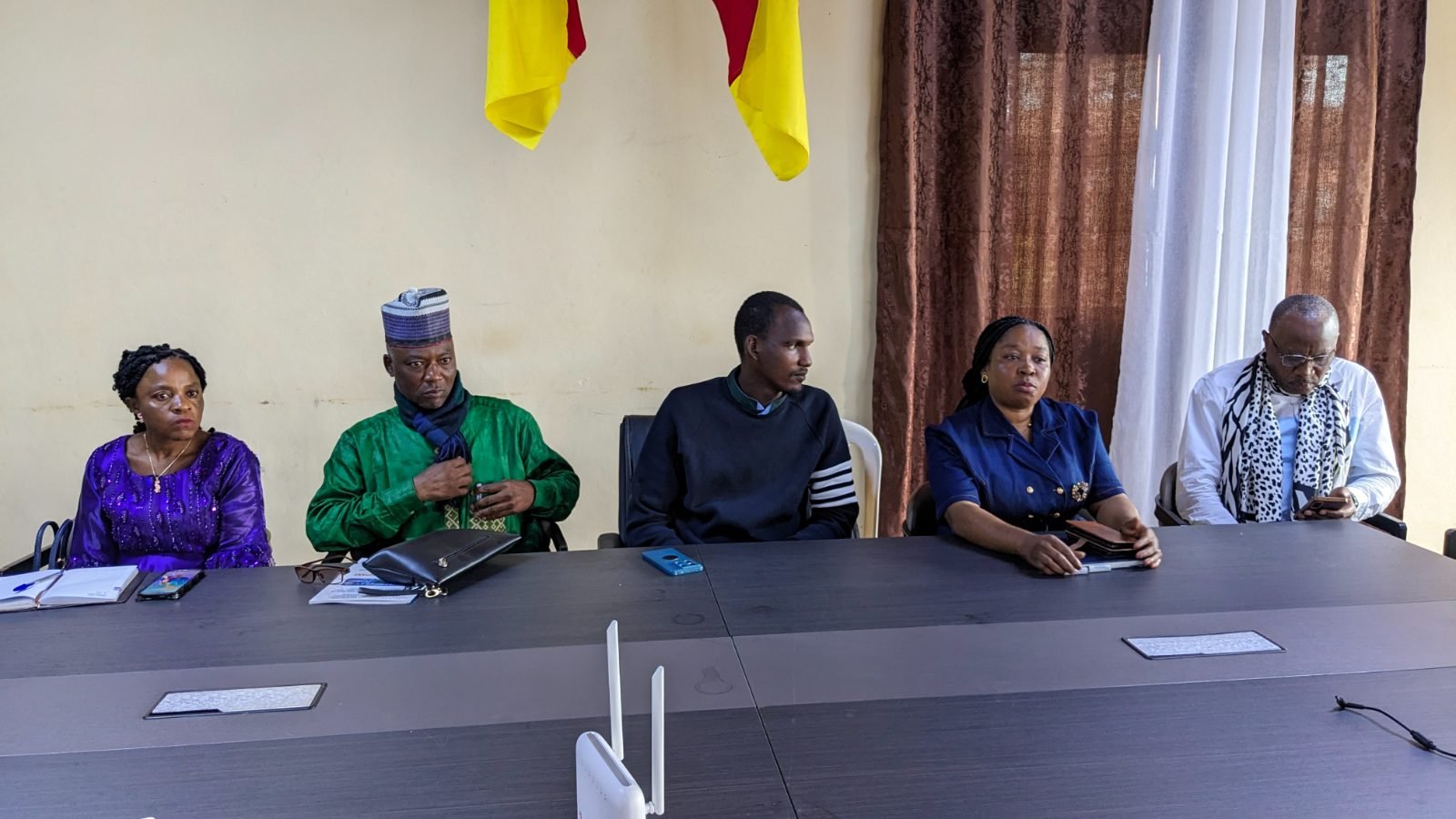 Cinq participants assis à la table de la salle de formation, sous des drapeaux du Cameroun.