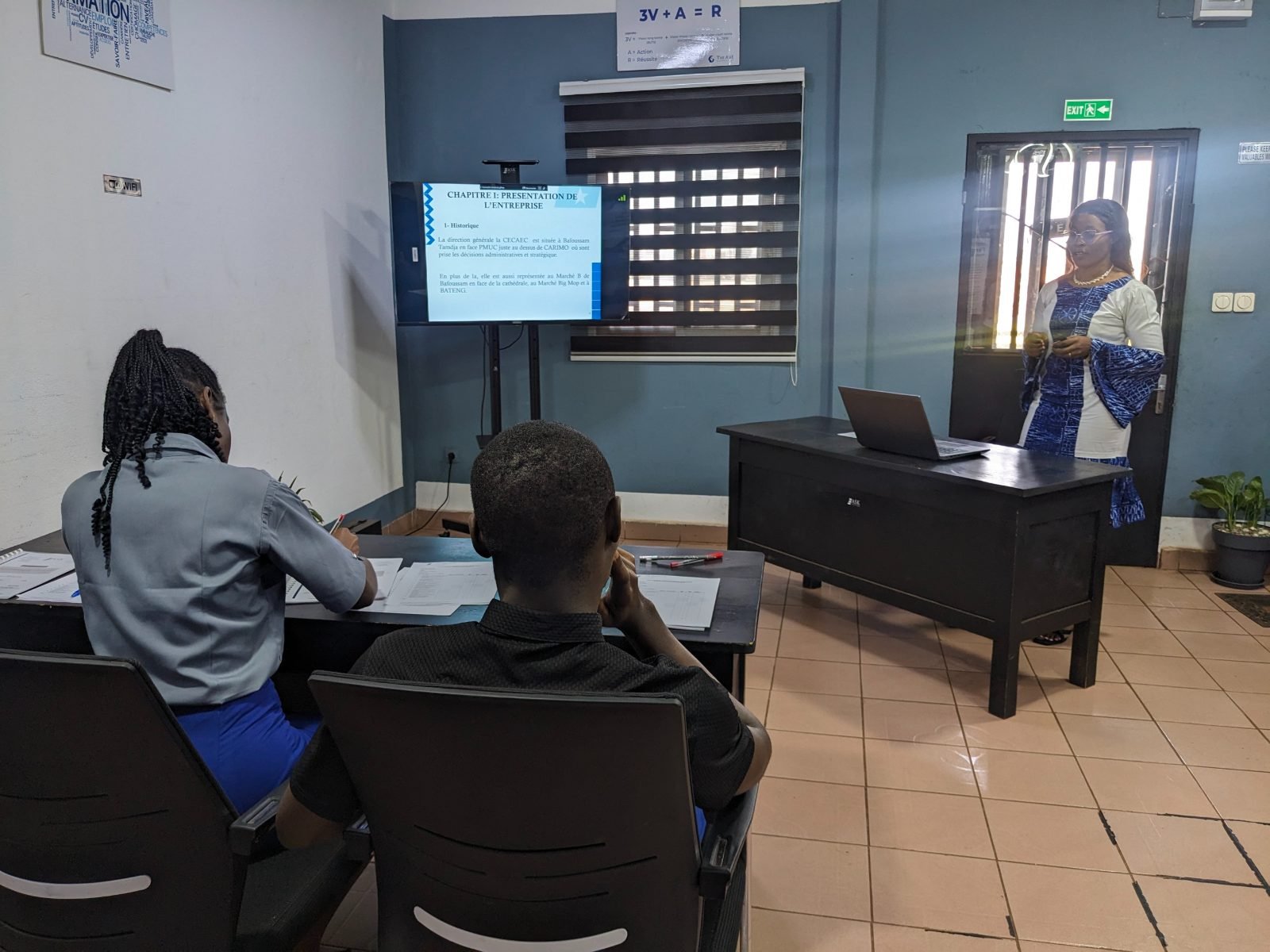 Face au jury, une apprenante en tenue bleue et blanche présente son rapport de stage ; l’écran affiche « Chapitre I : présentation de l’entreprise ».