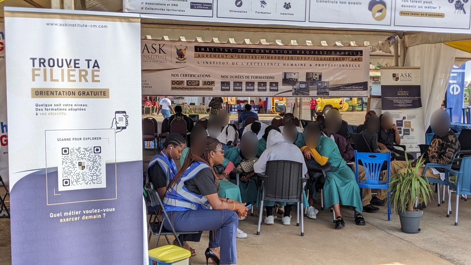 Sur le stand de ASK, deux membres de l’équipe en gilet conduisent une séance d’orientation avec un groupe d’élèves, près du kakémono « Trouve ta spécialité, orientation gratuite ».