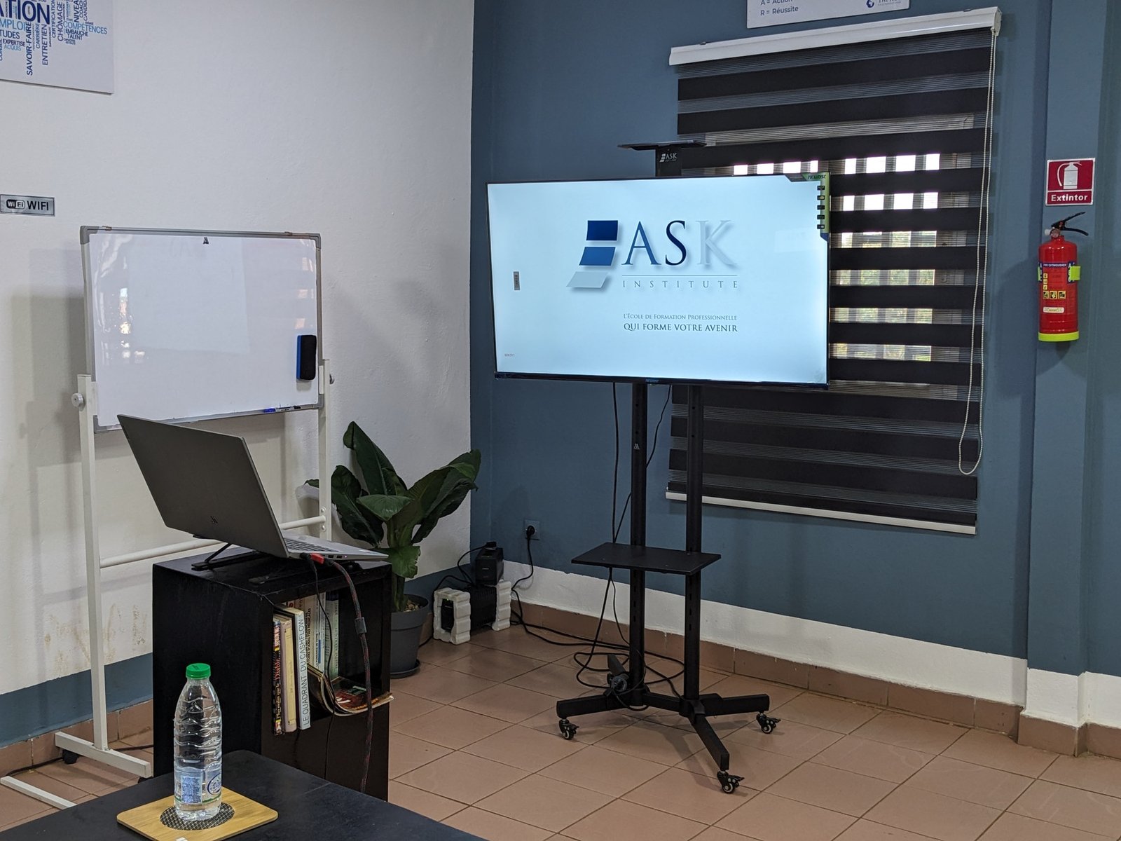 Écran pédagogique mobile et tableau blanc dans une salle de formation.