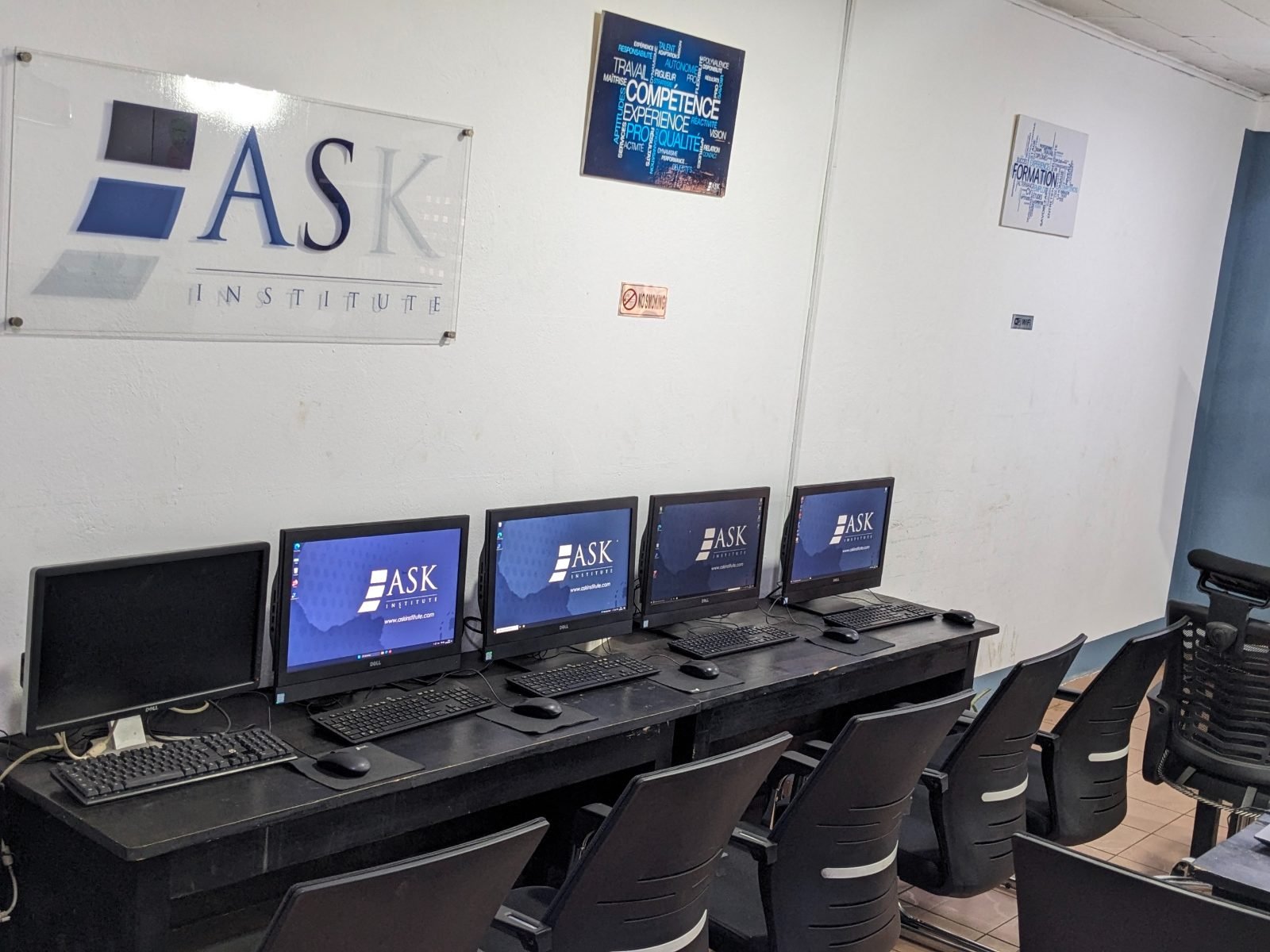 Salle informatique : une rangée de postes de travail sous le logo de ASK Institute.